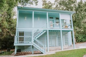 a blue house with a staircase in the grass at Blue Crest Architectural Treehouse Retreat in Ocean Springs