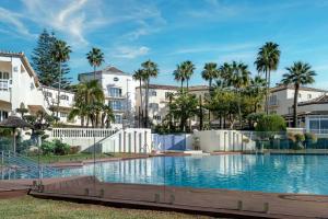 a swimming pool with palm trees and buildings at Grand Hotel Las Dunas, Autograph Collection in Estepona