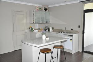 a kitchen with white cabinets and a counter with two stools at Parnwell Villa Apartment - The Tropical Oasis in Tauranga