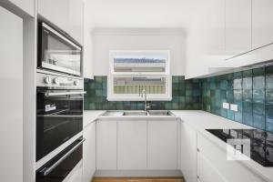 a white kitchen with a sink and a window at Garden Cottage Noraville in Toukley +24 photos