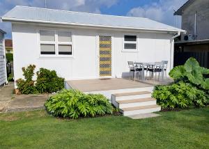 a white house with a table and chairs in a yard at Frangipani Hideaway in Budgewoi