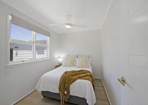 a white bedroom with a bed and a window at Frangipani Hideaway in Budgewoi