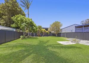 a backyard with a fence and a yard with green grass at Frangipani Hideaway in Budgewoi +8 photos
