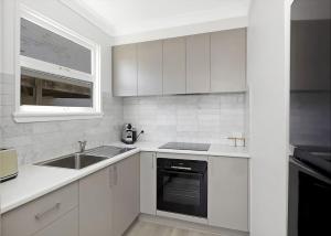a white kitchen with a sink and a dishwasher at Frangipani Hideaway in Budgewoi