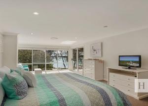 a white bedroom with a bed and a television at Enjoy Lazy Daze in Summerland Point