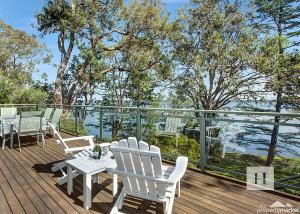 a deck with white chairs and a table and a view of the water at Niaroo Lakeside in Summerland Point