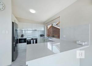 a white kitchen with white appliances and a large window at Sunset Lakehouse in Toukley
