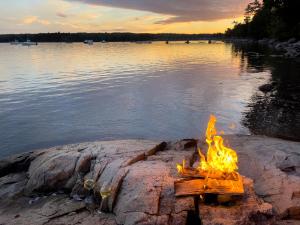 a campfire on the rocks near the water at Lucky Stone Retreat - private beach & Acadia view in Sullivan