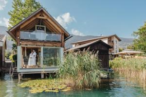 a couple stands in the window of a house on the water at Hotel SeeRose in Bodensdorf