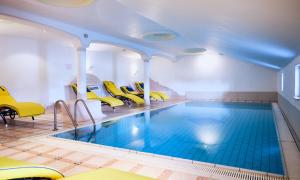 a swimming pool with yellow chairs in a room at Hotel Enzian by Alpeffect Hotels in Zauchensee