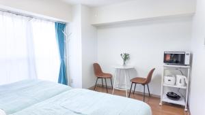 a white bedroom with a bed and two chairs at 9Stay川崎 in Kawasaki