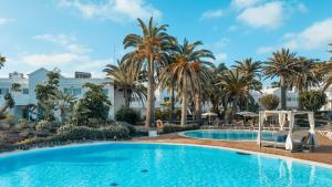 a pool with palm trees and a building at BLUESEA Corralejo Village in Corralejo