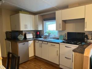 a kitchen with white cabinets and a sink and a microwave at Mobil Home avec WIFI -6-8 Personnes in Lattes
