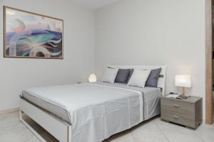 a white bedroom with a bed and a painting on the wall at Brezza di Mare Apartment in Scanzano
