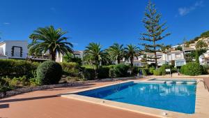 a swimming pool in a yard with palm trees and houses at Rosalalinda - cosy semi-detached home with sea views and large terrace in Moraira