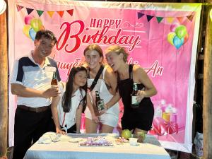 a group of people standing around a table with a happy birthday banner at Loren Homestay in Phong Nha