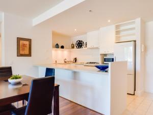 cocina con armarios blancos y mesa de madera en Waterfront (Yarra St) by Gold Star Stays en Geelong