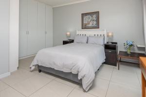 a white bedroom with a large bed and two tables at Fynbosrus on Grotto in Hermanus