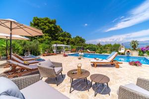 an outdoor patio with chairs and tables and a pool at Beachfront House Mir Brač near Supetar with pool and jacuzzi in Mirce