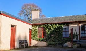 an ivy covered building with a red door and a bench at Strathpeffer Holiday Cottages in Strathpeffer
