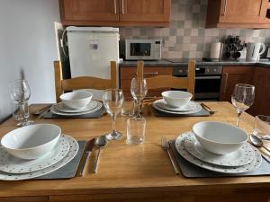 a wooden table with plates and bowls and wine glasses at Brada View - Bamburgh, Northumberland in Bamburgh