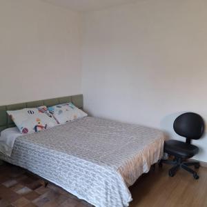 a bedroom with a bed and a black chair at Quarto aconchegante in Curitiba