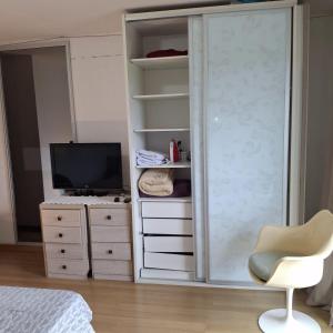 a bedroom with a cabinet and a tv and a chair at Quarto aconchegante in Curitiba