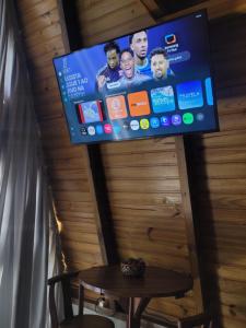 a flat screen tv on a wooden wall with a table at Hospedagem Chalés Prosas e Versos in Penha