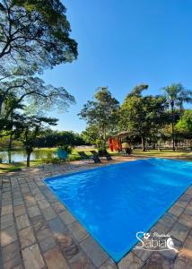 a blue swimming pool in a park with chairs and trees at Pousada Sabiá in Brotas