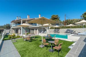 a house with a lawn with chairs and tables and umbrellas at Harmony Apartments in Agioi Apostoli
