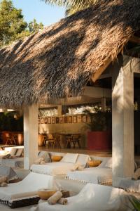 a row of beds in a room with a thatch roof at Esh Hotel & Spa, a Member of Design Hotels in Nosara