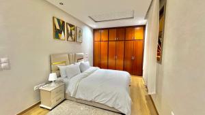 a bedroom with a white bed and a wooden cabinet at A2 Luxe Moderne et Confort, 7 min du Stade Moulay Abdellah in Temara