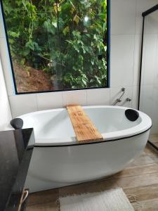 a white bath tub in a bathroom with a window at Chalé Studio Haven, microcasa com Mezanino e banheira in Lumiar +8 photos