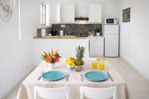 a white kitchen with a table with plates and fruit on it at T3 climatisé avec terrasse proche plages in Rivière-Pilote