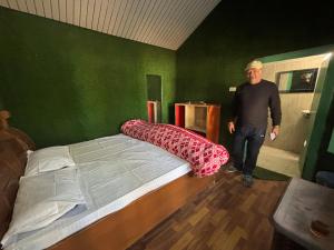 a man standing next to a bed in a room at Gauri Homestay in Pithorāgarh