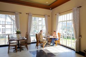 two people sitting at a table in a room with large windows at Grosvenor Hotel in Nuwara Eliya