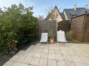 two white chairs sitting on a patio in front of a fence at Cottage with Garden 5mn Beach in Cabourg