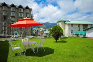 a table and chairs with a red umbrella in the grass at Grosvenor Hotel in Nuwara Eliya