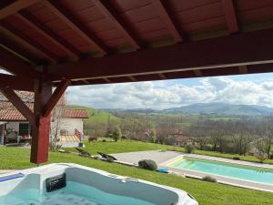 a hot tub under a pergola next to a swimming pool at Le cocon Laina Piscine & spa optionnel in Irissarry