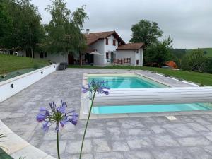 a swimming pool in front of a house with purple flowers at Le cocon Laina Piscine & spa optionnel in Irissarry