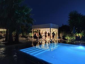 a group of people standing around a pool at night at NOBILIS CORFU Hotel in Acharavi