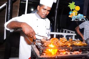 a man cooking food on a grill with a spatula at Dinuda Lagoon Hotel in Kalpitiya