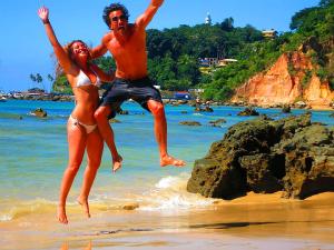 a man and woman jumping in the water on the beach at Pousada VillaBahia Morro in Morro de São Paulo