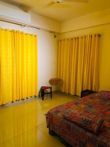 a bedroom with yellow curtains and a bed and a table at Pakhir Basha in Dhaka