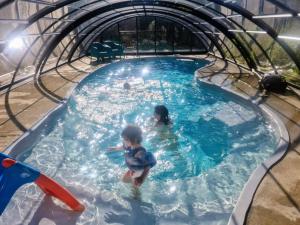 a couple of children playing in a swimming pool at La maison bleue avec une grande piscine chauffée in Bozouls