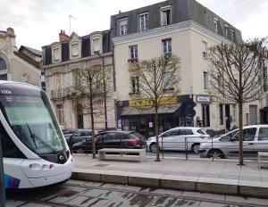 a train on a city street with parked cars at Hôtel Du Mans in Angers