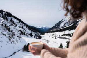 a woman holding a cup of coffee in the snow at Wohlfühlhotel Hubertushof am Arlberg - Ski-In & Ski-Out - Sky Pool in Stuben am Arlberg