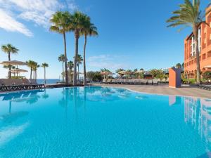 ein großer Swimmingpool mit Palmen und dem Meer in der Unterkunft H10 Tindaya in Costa Calma