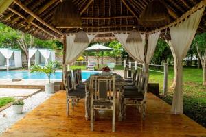 a dining table and chairs under a pergola next to a pool at BREEZEACARDEs in Diani Beach