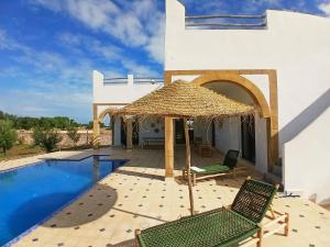 a villa with a swimming pool with two chairs and a straw umbrella at Chambres Maison d'hôtes MaisonBlanche in Essaouira